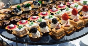An assortment of small desserts, including cakes topped with berries, whipped cream, and chocolate, elegantly displayed on a glass tray—perfect for a creative food station at any corporate event.
