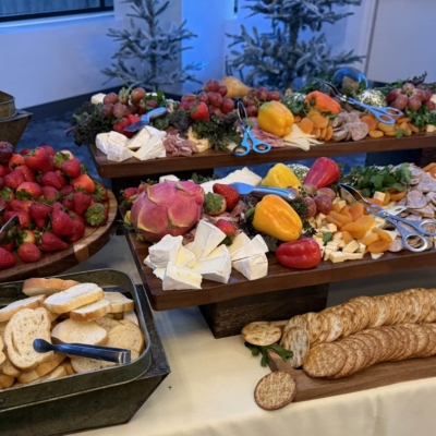 A table with an assortment of breads, crackers, cheeses, fruits, meats, and vegetables arranged on trays for a beautiful charcuterie board perfect for buffet-style catering services.