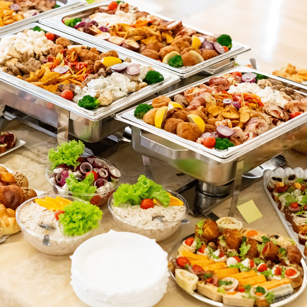 Buffet table with trays of assorted hot dishes, salads, and garnished appetizers, with plates stacked in the foreground—perfect for lunch catering or catering services in Orem Utah.