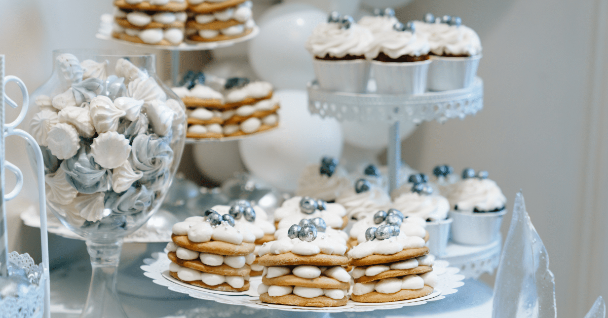 Dessert display featuring cupcakes and layered cookies topped with white frosting and silver decorations, alongside a glass vase filled with white and silver meringues—perfect for Utah Catering's seasonal wedding menus.
